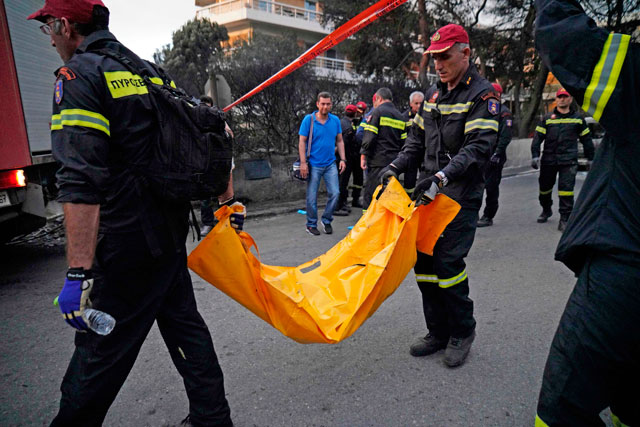 Firefighters carry a dead person following a wildfire at the village of Mati, near Athens, on Tuesday  (AFP photo)