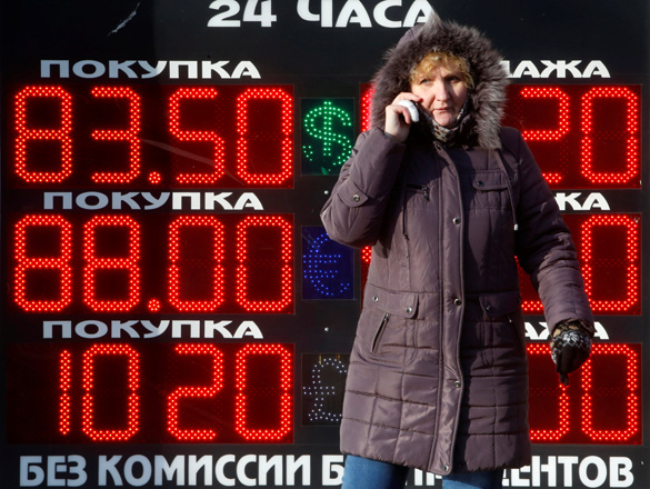 A woman uses a mobile device near a board showing currency exchange rates of the US dollar, euro and the British pound against the rouble in Moscow, Russia, on January 21, 2016 (Reuters file photo)
