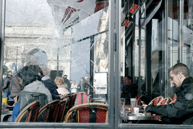 People sit at the terrace of a restaurant are seen behind a damaged window on the Champs-Elysees avenue in Paris on Sunday, a day after the 18th consecutive Saturday of demonstrations called by the ‘Yellow Vest’ (gilets jaunes) movement (AFP photo)