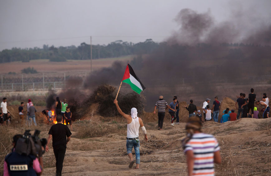 Protesters, one holding Palestinian flag, confront Israeli soldiers by the Israeli border with Gaza in Buriej, central Gaza Strip, Thursday (AP photo)