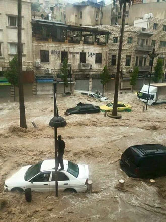 An Amman resident stands on top of his car as floodwaters surround other vehicles in the neighbourhood on Thursday (Al Rai photo)