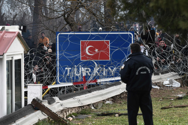 A Greek police officer faces migrants gathered at the Greece-Turkey border, near Kastanies, Greece, on Saturday (AFP photo)