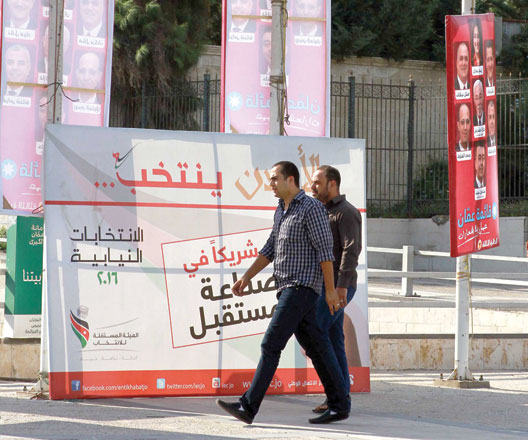 Men walk past campaign posters with pictures of candidates for the September 20 parliamentary elections in Amman on Wednesday (Photo by Hassan Tamimi)