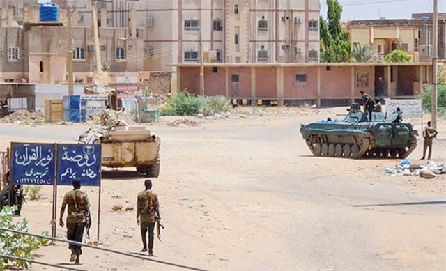 Sudanese army soldiers walk near armored vehicles positioned on a street in southern Khartoum, on May 6, 2023 (AFP photo)