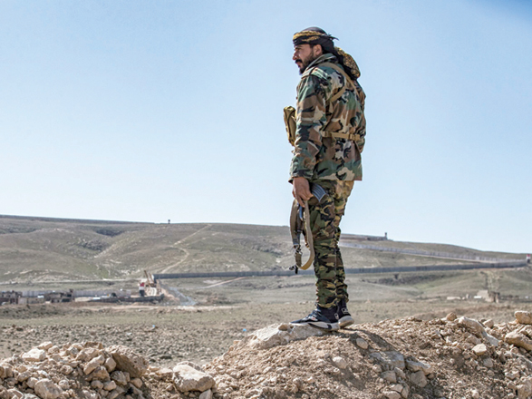 A member of the border guard force loyal to the Syrian Democratic Forces looks on near Syria's town of Al Hol at ongoing construction of a concrete border fence being erected on the Iraqi side (AFP file photo)
