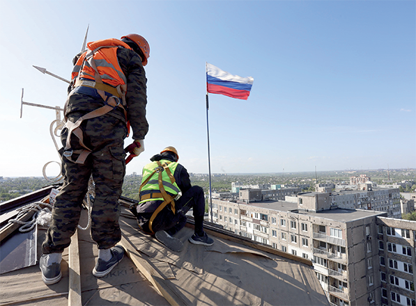 Workers repare a roof, as Russian flag waves over Mariupol, Russian-controlled Ukraine, on Monday, amid the Russia-Ukraine conflict (AFP photo)