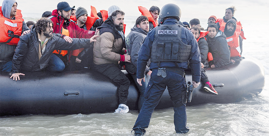 Migrants react as a French police officer stands by ready to puncture the smuggler’s boat with a knife to prevent migrants from embarking in an attempt to cross the English Channelon the beach of Gravelines, near Dunkirk, northern France on Friday (AFP photo)