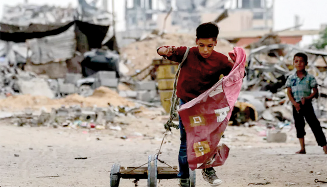 A boy pulls a cart with a rope while walking past a destroyed building in Khan Yunis in the southern Gaza Strip on October 7 (AFP photo)
