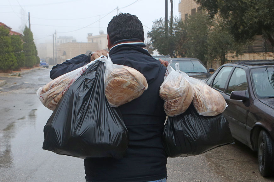A man carries a load of bread and other items in Amman under rain on Sunday. A snowstorm was expected to last for three days  (Photo by Khalid Oudat)
