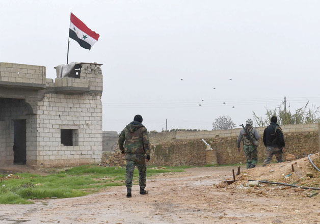 This photo taken on Monday shows a Syrian national flag flying over a building as regime forces gather in the southern countryside of the northern Kurdish-controlled city of Manbij (AFP photo)