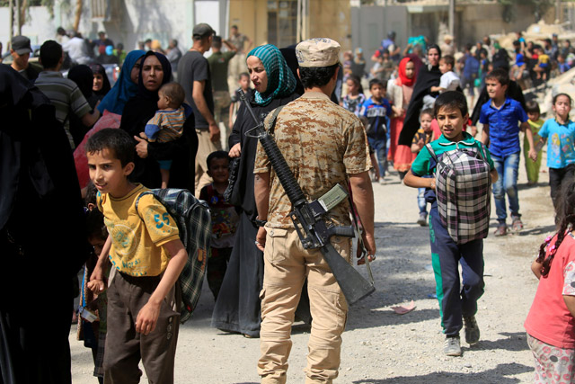 A member of Iraqi Rapid Response forces stands guard while displaced Iraqi people who fled from clashes walk in western Mosul, Iraq, on Saturday (Reuters photo)