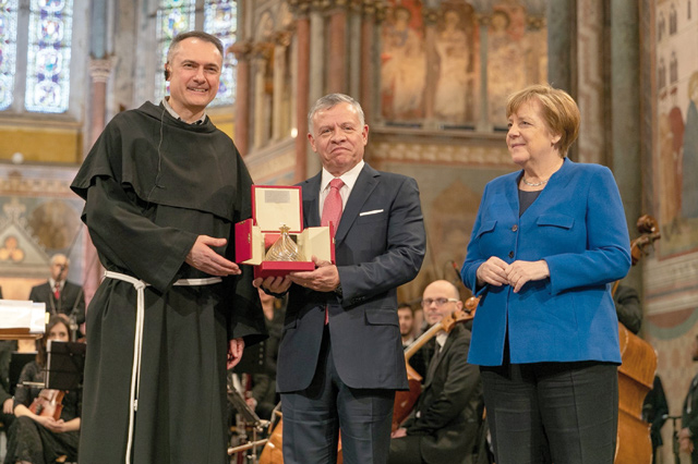 His Majesty King Abdullah receives the 2019 Lamp of Peace award from Sacred Convent Custodian Father Mauro Gambetti (left), in the presence of German Chancellor Angela Merkel (right), on Friday, in Assisi, Italy (Photo courtesy of Royal Court)