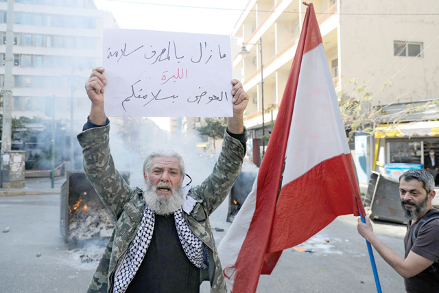 An anti-government demonstrator carries a placard which reads 'The bank is safe, the currency is dead' block the street, with burning garbage dumpsters, in front of Lebanon's central bank in the capital Beirut on Tuesday, during a protest against the deteriorating economic situation (AFP photo)