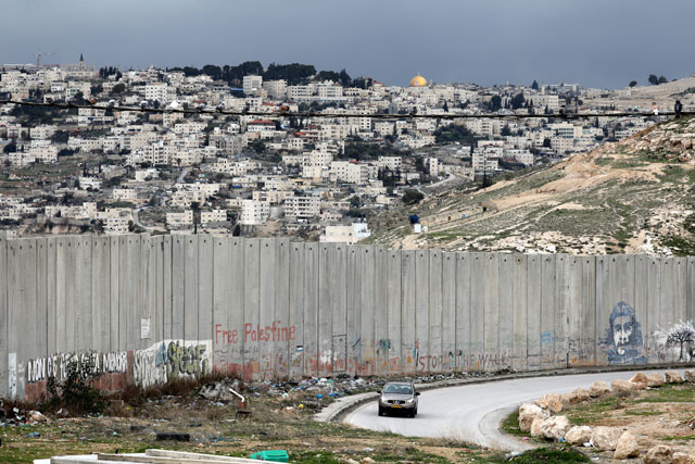 A car drives along a road near the Israeli separation barrier in the Palestinian town of Abu Dis in the West Bank, as Jerusalem is seen in the background, on Wednesday (Reuters photo)