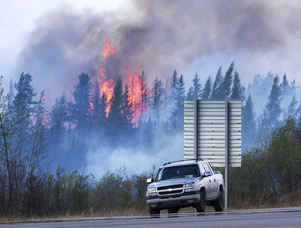 Flames flare up from hotspots from a wildfire along a highway to Fort McMurray, Alberta, Canada, May 8. In Canada devastating wildfires near Fort McMurray forced a shutdown of 1.2 million barrels a day of production early this month (AP photo)