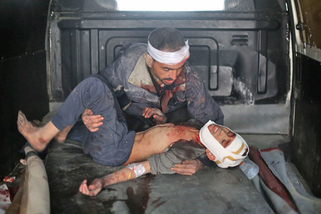 A wounded man carries a wounded child upon their arrival at a makeshift hospital in Zamalka, near Damascus on Monday, following reported air strike (AFP photo)