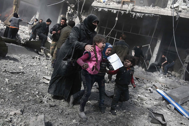 A Syrian woman and children run for cover amid the rubble of buildings following government bombing in the rebel-held town of Hammuriyeh, in the besieged Eastern Ghouta region on the outskirts of the capital Damascus, on Monday (AFP photo)