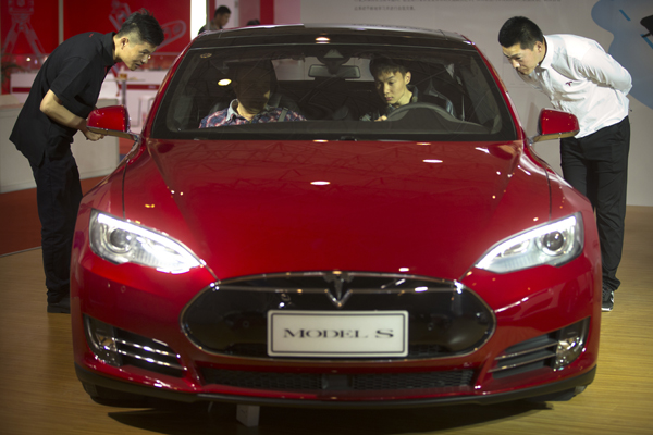 Staff members talk with visitors as they sit inside a Tesla Model S electric car on display at the Beijing International Automotive Exhibition in Beijing, on Monday (AP photo)
