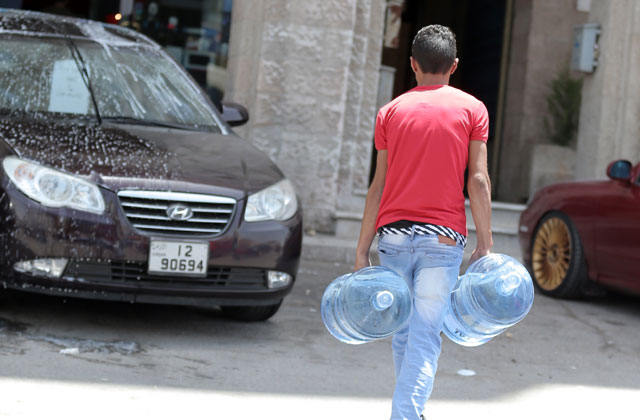 A man walks down a street in Amman while carrying water bottles on Thursday, which witnessed a slight rise in temperatures (Photo by Osama Aqarbeh)