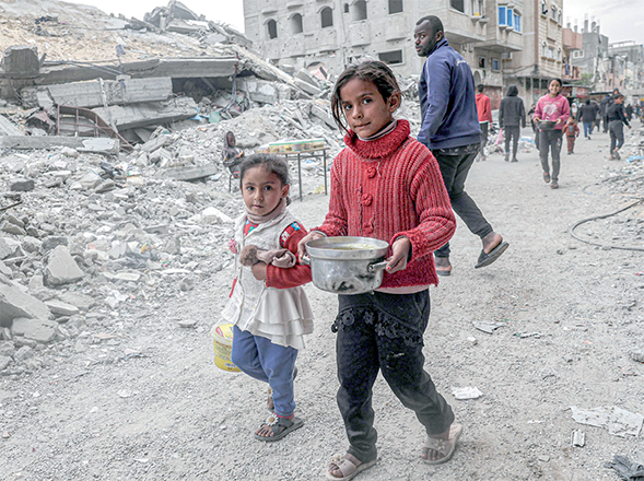 Children walk past the rubble of a collapsed building with a pot of food provided by a charity organisation ahead of the fast-breaking ‘Iftar’ meal during the Muslim holy month of Ramadan, in Rafah in the southern Gaza Strip on Saturday (AFP photo)