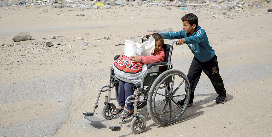 A boy pushes a young girl in a wheelchair past a destroyed building in Gaza City on Thursday, amid the ongoing Israeli war against the coastal enclave (AFP photo)
