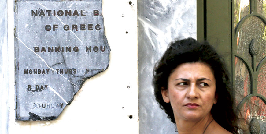 A Greek woman pauses by a broken marble National Bank sign outside a branch in Athens on Wednesday (Reuters photo Yannis Behrakis)