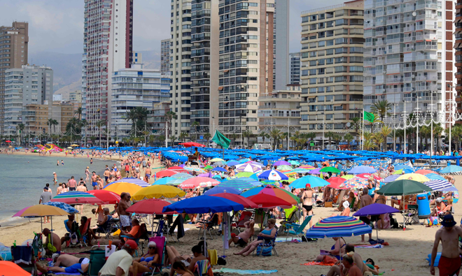 In this file photo taken on June 7, sunbathers walk by the sea on Levante Beach in Benidorm, on the Mediterranean coast of Spain (AFP photo)
