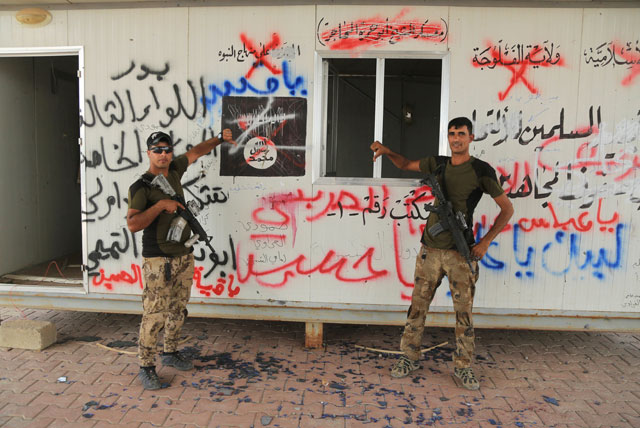 In this Thursday photo, Iraqi soldiers stand in front of graffiti in Arabic that reads: ‘The state of Fallujah’, ‘Sheikh Abu Hamza Al Muhajir Camp’, ‘On a platform of prophecy’, ‘O Abbas’, ‘O Hussein’, ‘Beck O Ali’ and ‘Muhammad is the Messenger of Allah’ in Fallujah, Iraq (AP photo)