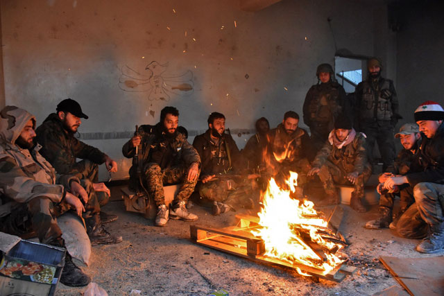 Syrian pro-government forces rest by a fire as they advance in the Jisr Al Haj neighbourhood during the ongoing military operation to retake remaining rebel-held areas in the northern embattled city of Aleppo, on Wednesday (AFP photo)