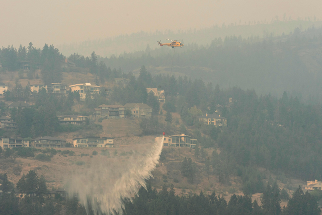 A helicopter drops water as the McDougall Creek wildfire continues to burn in West Kelowna, British Columbia, on Saturday. Around 30,000 people were under orders on Saturday to evacuate their homes in western Canada's British Columbia, provincial officials said, as a raging wildfire bore down on the city of Kelowna (AFP photo)