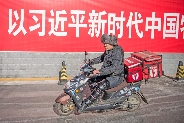 A man rides his scooter past a board that reads, ‘For a new era in China with Xi Jinping’ in Beijing on Thursday (AFP photo)