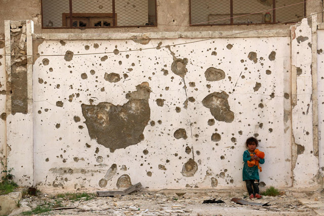 A displaced Syrian girl plays with a cuddly toy in front of a damaged wall in the city of Azaz, situated on the border with Turkey, on Sunday (AFP photo)