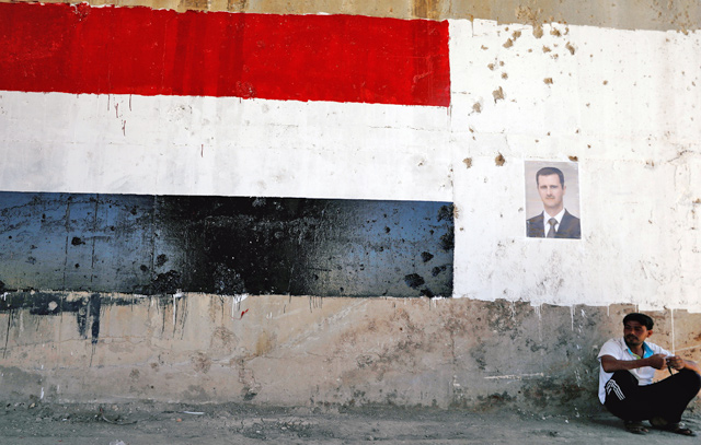 A man sits near a poster of Syrian President Bashar Assad during the re-opening of the road between Homs and Hama in Talbisi, Syria, on Wednesday (Reuters photo)