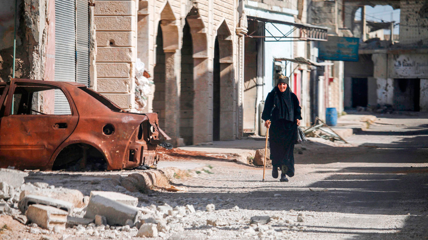A Syrian woman walks with a cane past a destroyed car down a street in Al Hirak in the eastern Daraa province countryside on Thursday (AFP photo)