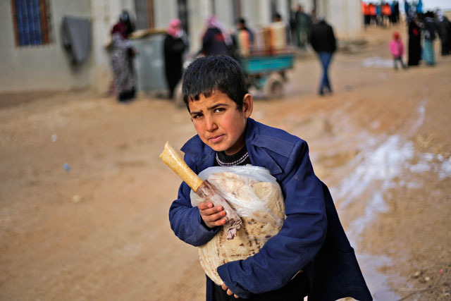 A Syrian boy displaced with his family from eastern Aleppo holds a sandwich and bread bag in the village of Jibreen, south of Aleppo, Syria, on Saturday (AP photo)