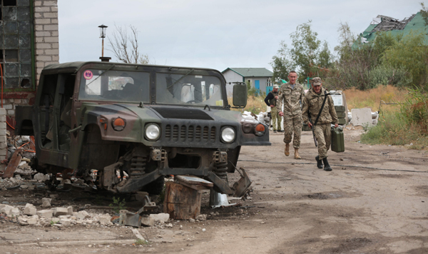 Ukrainian servicemen walk past the wreckage of a military car destroyed by pro-Russian separatists shelling in the small town of Shyrokyne in Donetsk region, on August 14 (AFP photo)