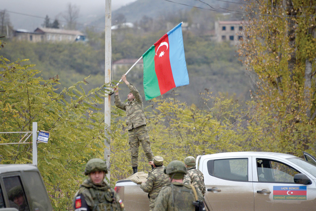 An Azerbaijani soldier fixes a national flag on a lamp post in the town of Lachin on Tuesday (AFP photo)