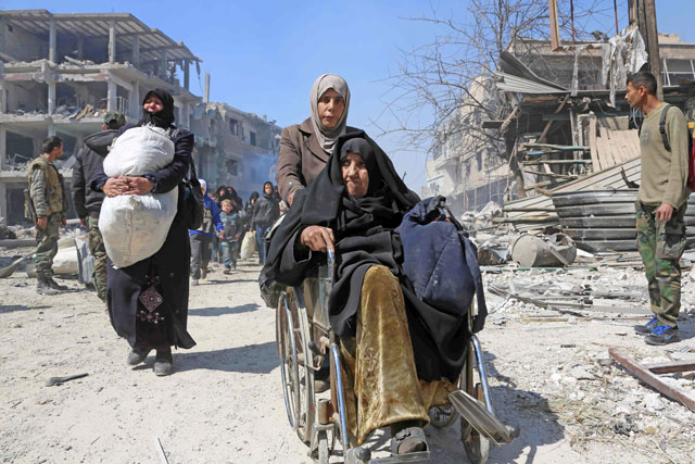 A Syrian woman sitting in a wheelchair is pushed during a civilian evacuation from the town of Jisreen in the southern Eastern Ghouta, on the eastern outskirts of the capital Damascus, on Saturday (AFP photo)