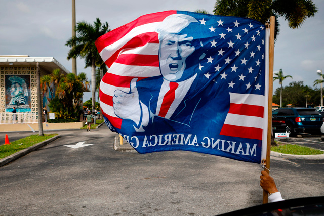 A supporter holds a flag depicting US President Donald Trump's face at the parking of John F. Kennedy Public Library as voters cast their early ballots in Hialeah, Florida, on Monday (AFP photo)