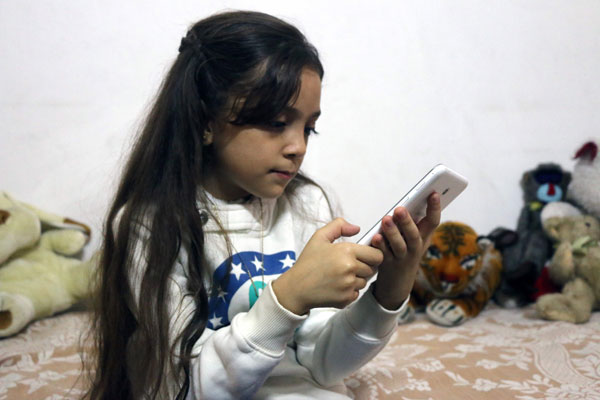 Syrian Bana Al Abed, who with the help of her mother had been posting heart-rending tweets in English on life in the besieged eastern districts of Syria’s Aleppo, uses a smartphone to check her Twitter account in her home in east Aleppo, on October 12 (AFP photo)