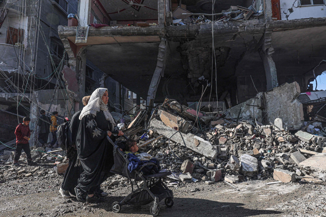 Palestinians walk past building rubble following Israeli air strikes on the Rafah refugee camp in the southern Gaza Strip on Saturday (AFP photo)