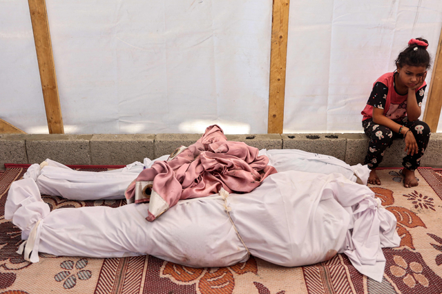 A girl sits by the retrieved bodies of victims killed in the aftermath of overnight Israeli bombardment at the Asma school run by UNRWA, in the Shati camp for Palestinian refugees west of Gaza City, on June 25, 2024 (AFP photo)