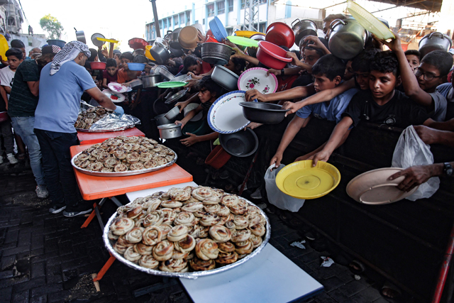 Palestinian children hold out their plates toward a man, to receive their share of vegetable patties prepared by volunteers in Beit Lahia in the northern Gaza Strip on Wednesday (AFP photo)