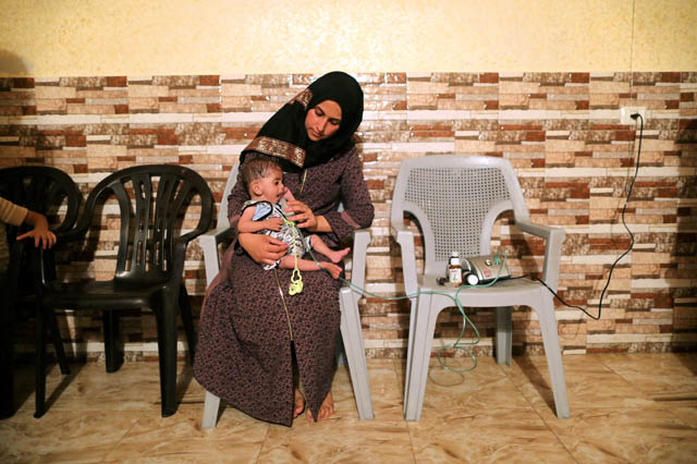 Palestinian boy Fares Al Jalees, who suffers from cystic fibrosis, is held by his mother Ritta as he receives oxygen supplementation therapy inside their house in Gaza City on July 2 (Reuters photo)