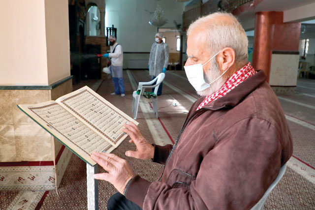 An elderly man wearing a face mask reads from the Holy Koran while seated in a mosque being sterilised by Palestinian health workers in the West Bank city of Ramallah on Saturday due to fears of coronavirus spread (AFP photo)