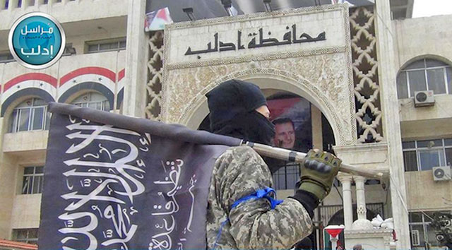 In this file photo posted on the Twitter page of Syria's Al Qaeda-linked Nusra Front on March 28, 2015, which is consistent with AP reporting, a fighter from Syria's Al Qaeda-linked Nusra Front holds his group flag as he stands in front of the governor building in Idlib province, north Syria (AP photo)