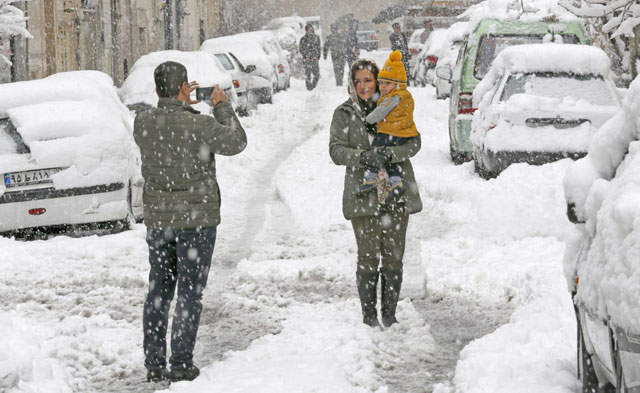 An Iranian man takes a photo of a woman and a child amid the snow in the capital Tehran on Sunday. (AFP photo)