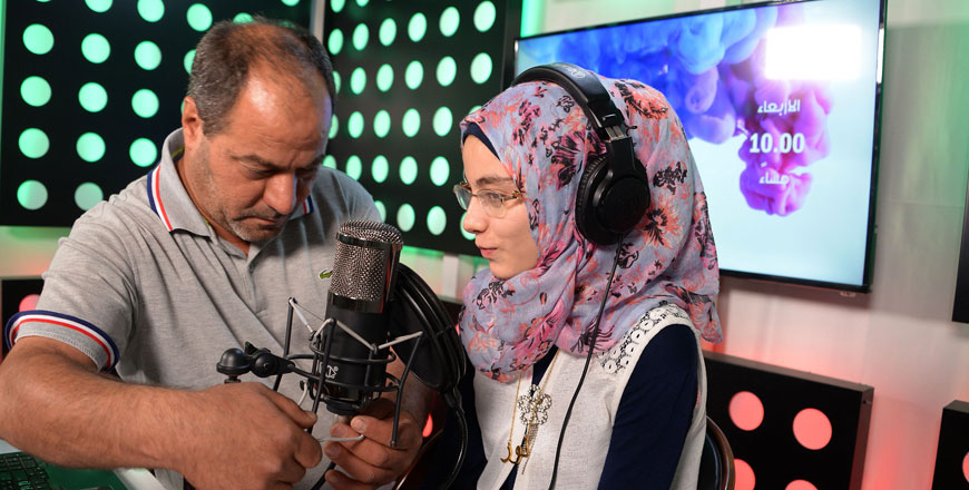 The father of radio presenter Nour Tai adjusts her microphone before she begins broadcasting her weekly programme on One FM, a radio station in the northern Iraqi city of Mosul, on May 30 (AFP photo)