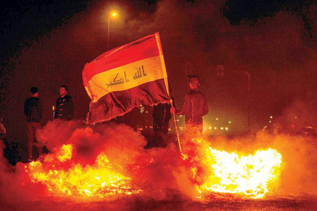 An Iraqi anti-government protester holds a national flag as he stands by a fire at a makeshift roadblock in the southern city of Basra late on Wednesday (AFP photo)