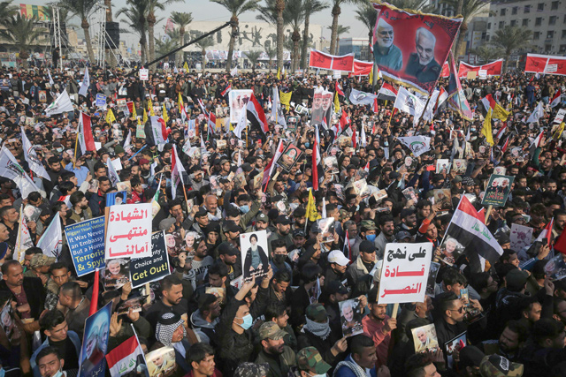 Iraqi demonstrators lift flags and placards as they rally in Tahrir Square in the capital Baghdad on Sunday, to mark one year after a US drone strike killed Iran's revered commander Qasem Soleimani and his Iraqi lieutenant Abu Mahdi Al Muhandis near the capital (AFP photo)